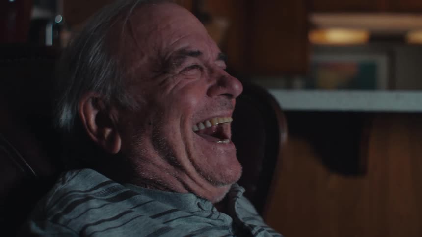 Elderly man sitting and laughing while watching TV
