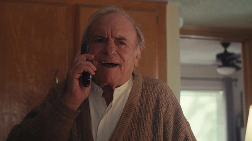 A man leans as he talks on his phone at home