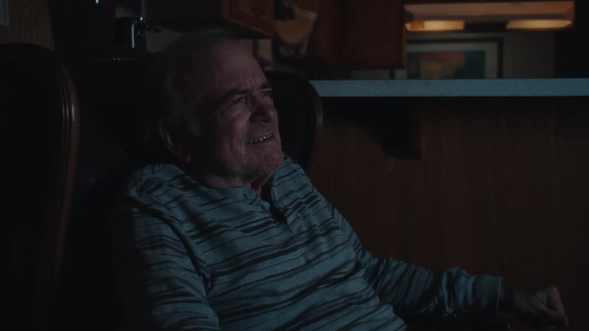Elderly man sitting in an armchair in a dark room watching