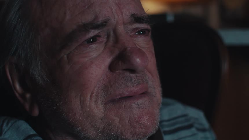 Close up of the face of a sad elderly man crying while watching TV at night