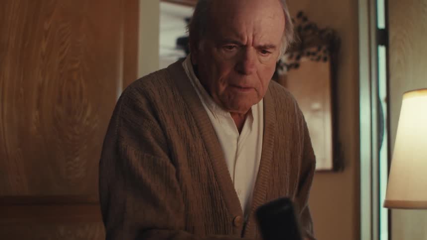 Elderly man sitting down gets up and answers a phone