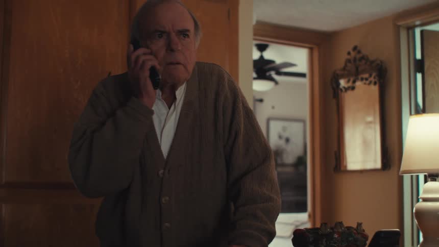 Elderly man walking around the room picking up the phone and answering a call