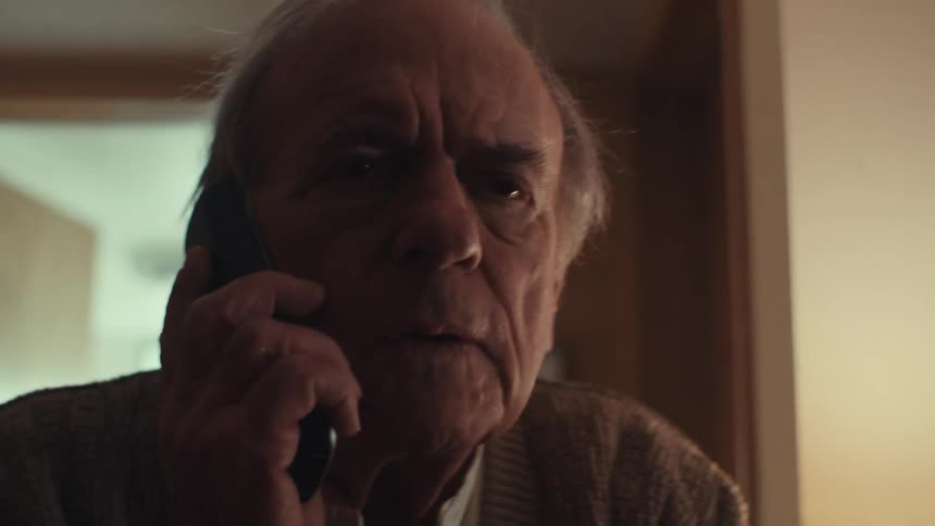 An elderly man stands up from bed to pick up the phone at home