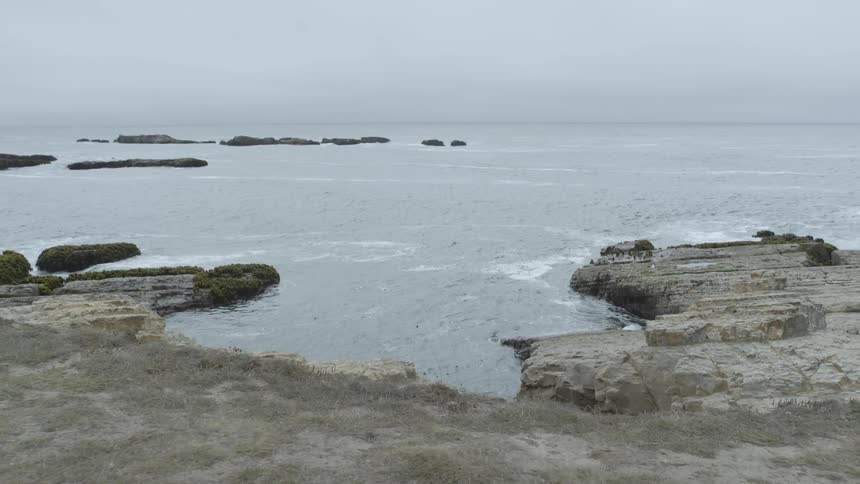 The tide beats against rocks below a cliff overlook on a cloudy day