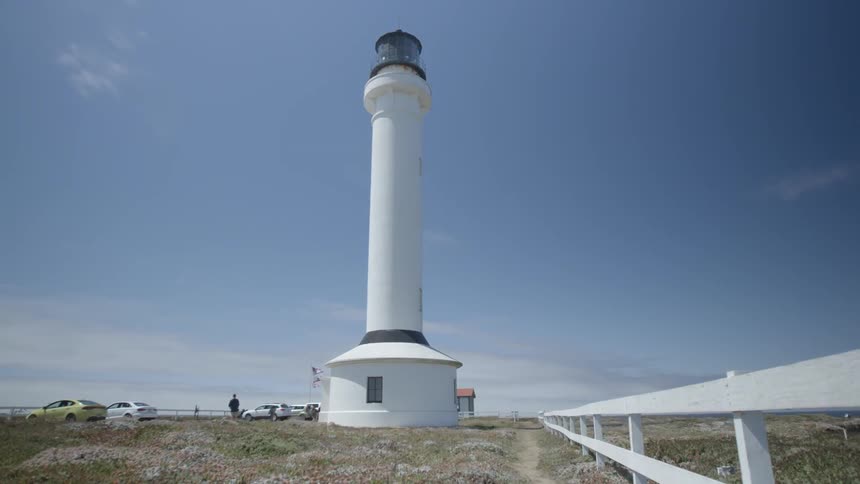 A person is standing in a parking lot next to a lighthouse
