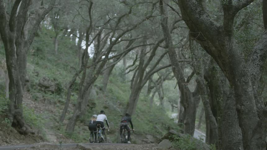 Three people ride their bikes on a trail by a hill