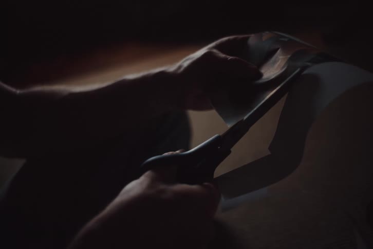 Closeup of a man cutting out a photograph with scissors