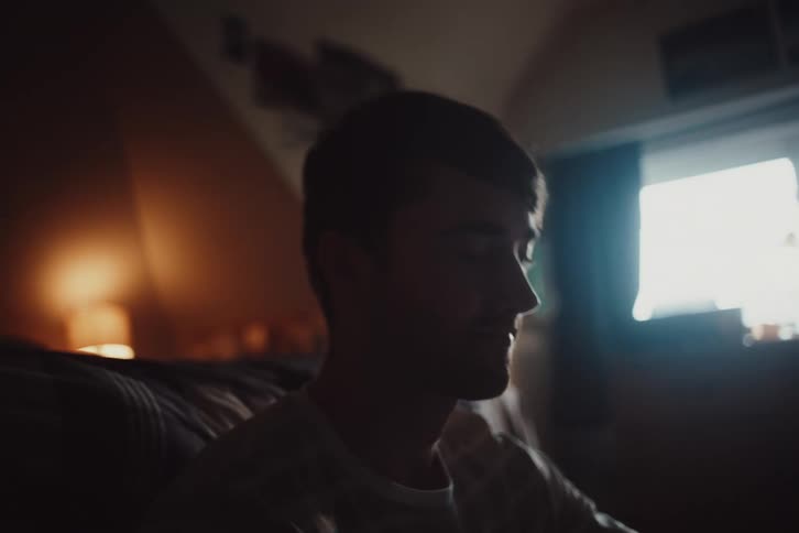 Close up of a young man sitting on a couch in a dimly lit room