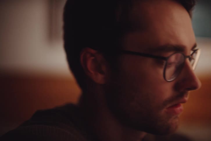 A close up profile view of a man wearing glasses with soft warm lighting