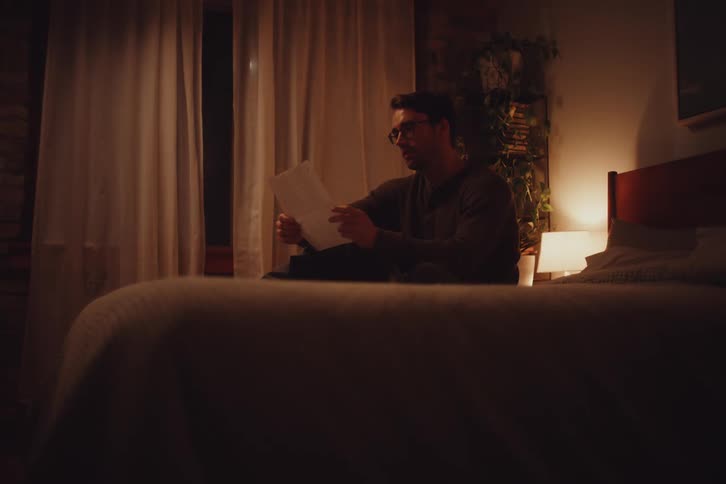 Man sitting on his bed at night reads