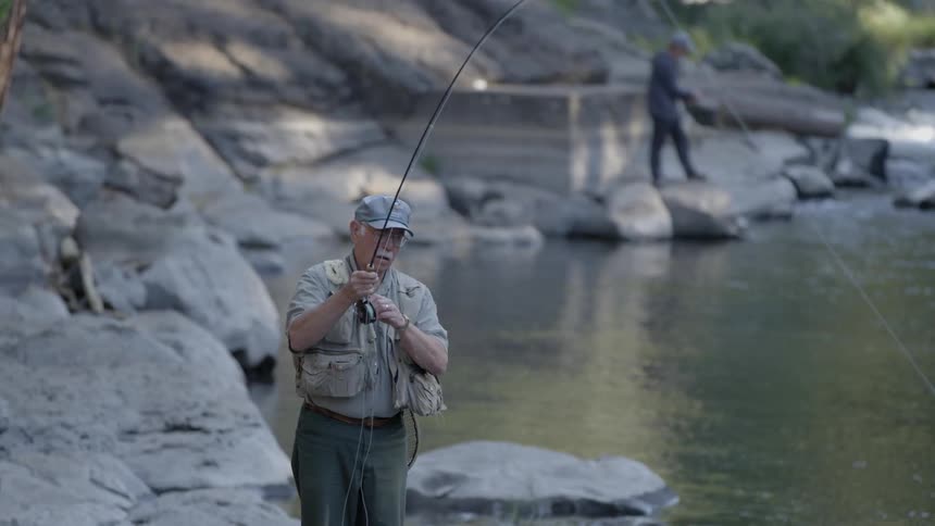 A fisherman reels in his line while standing on a boulder