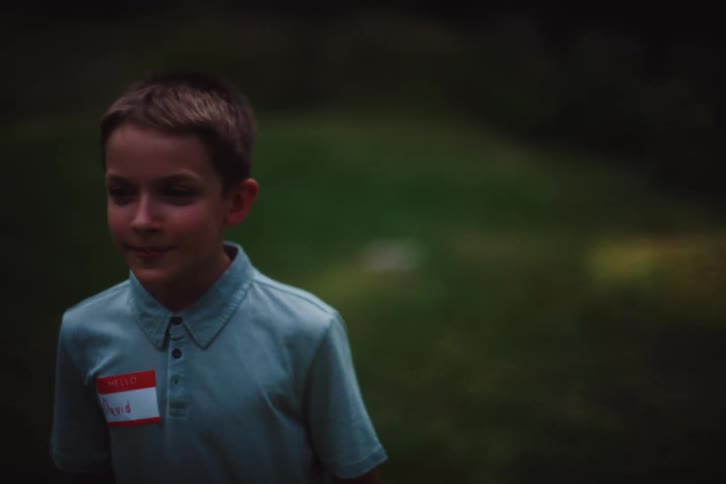 A boy in a light blue shirt laughs in the green field