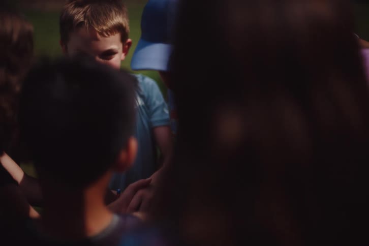 Several children are gathered together with their arms on top of each other and then a little boy leaves when a girl arrives