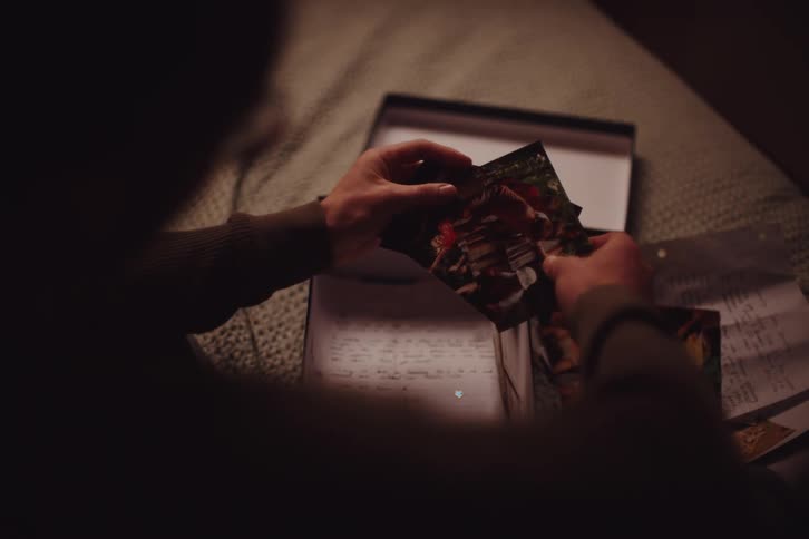 Man sits on a bed looking through photographs of children at a camp