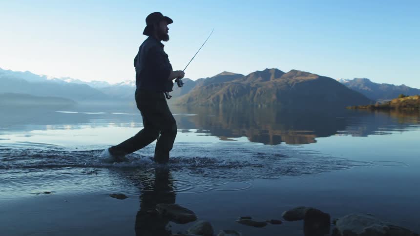 Man walking in water as he fishes at same time