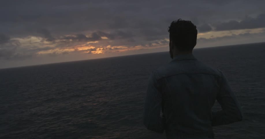 Men looking out at the water from the beach's edge at a cloudy sunset