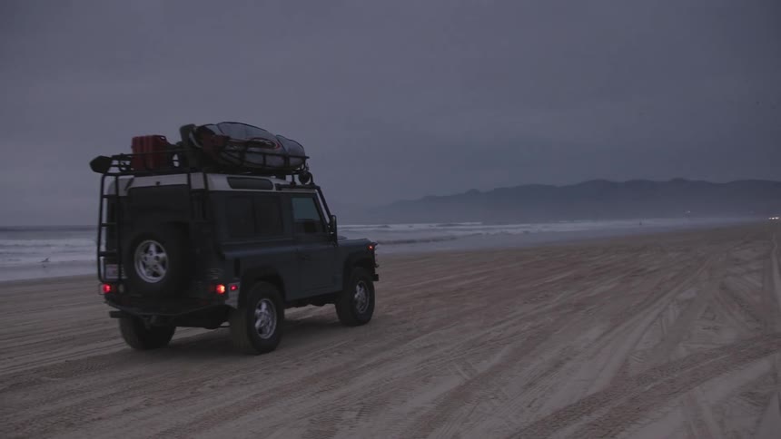 A jeep driving along a beach at dusk