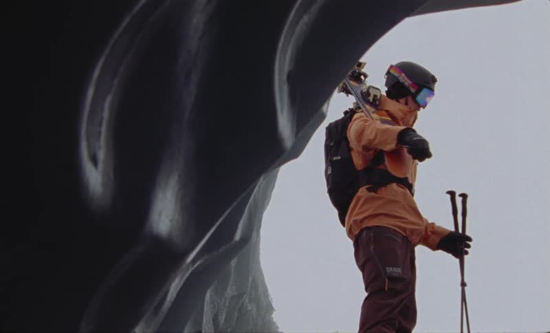 Woman standing at the entrance of a snow cave with her skis and poles