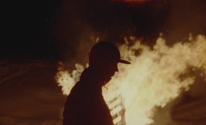 Side silhouette of a person next to an object on fire at night