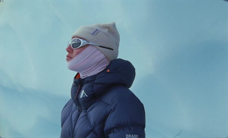 Person in blue winter jacket hat and glasses exploring a natural area with glaciers