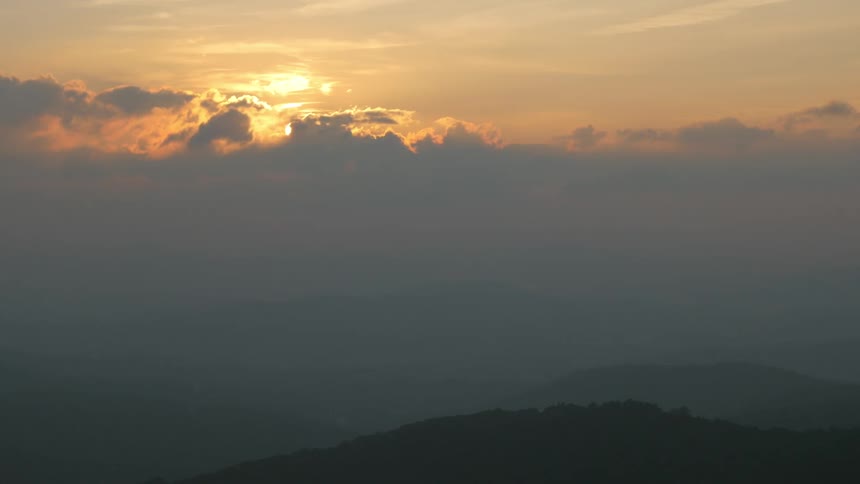 The sun coming up behind a cloud in the mountains