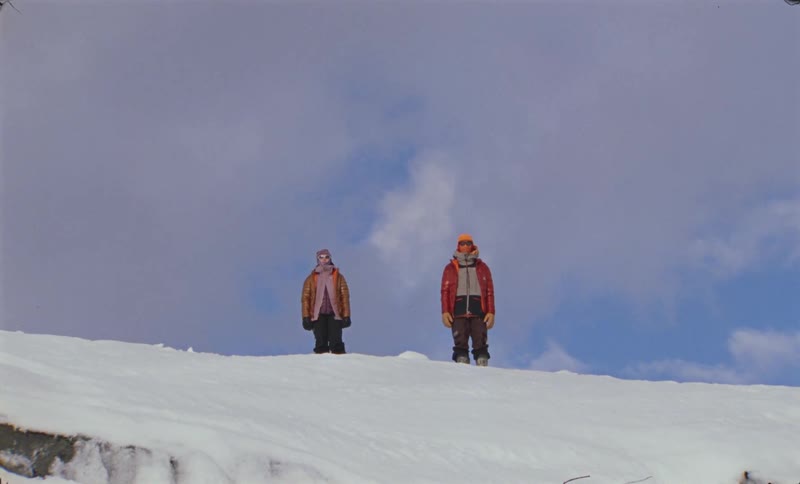 Two men bundled up for the cold stand on top of a snow covered mountain