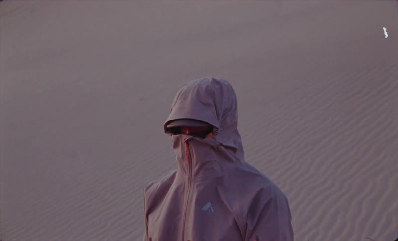 Man stands in a desert with his jacket zipped up to cover most of his face
