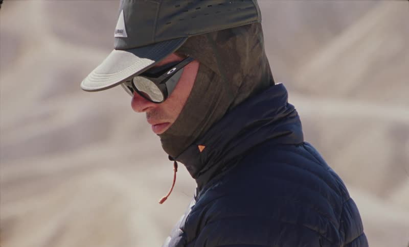 Man in a balaclava and coat stands in the desert