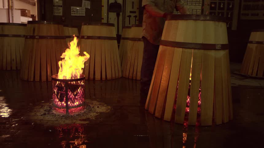 A person taking a wooden frame that is around a fire in a metal container and placing it in another one that is on the right side