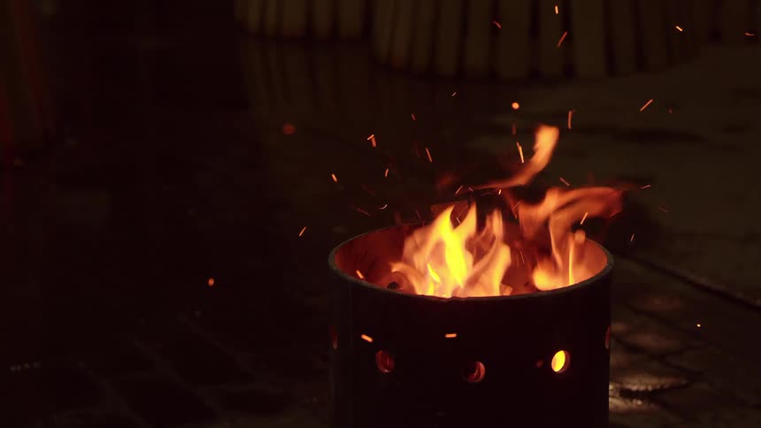 Wood is dropped into an already flaming fire pit on a brick patio
