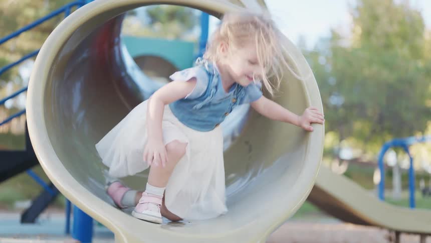 Little girl playing and going down a slide in a playground