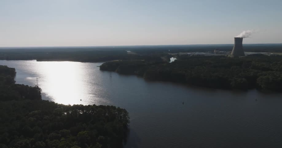 Large body of water reflecting sunlight with a nuclear power plant in the background