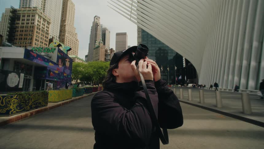 Man with a camera pointing upwards while standing on the streets of a metropolis