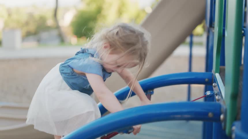 A toddler girl in a denim dress and white skirt plays on a blue playground structure