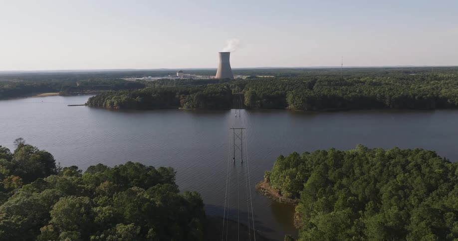 Nuclear power plant in the background with a cooling tower emitting steam and a large body of water surrounded by dense forest