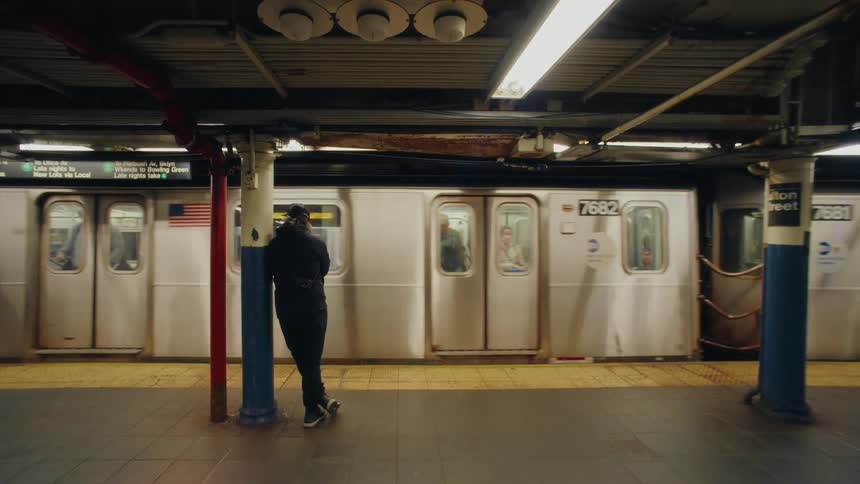 A person is standing with his back against a pillar in a terminal looking at a subway that is moving