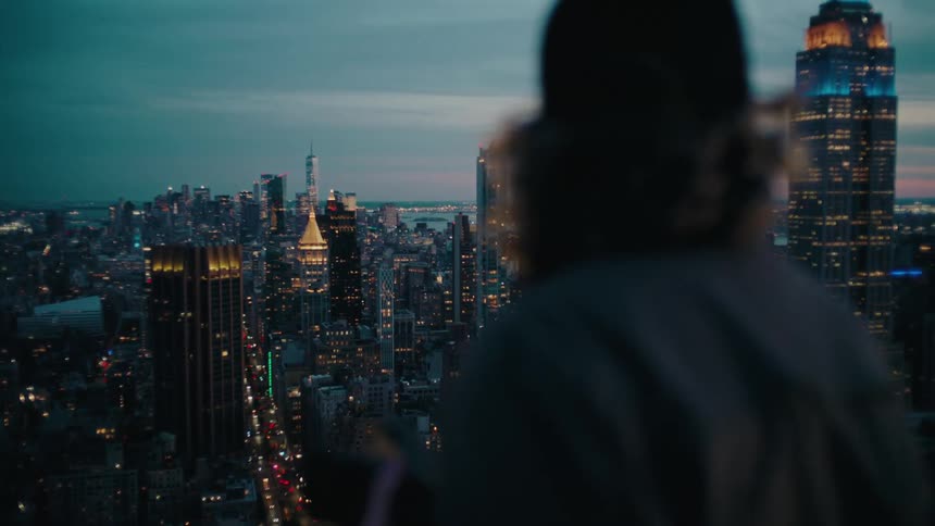A view of a vibrant city skyline as seen from above at dusk as a person looks over it