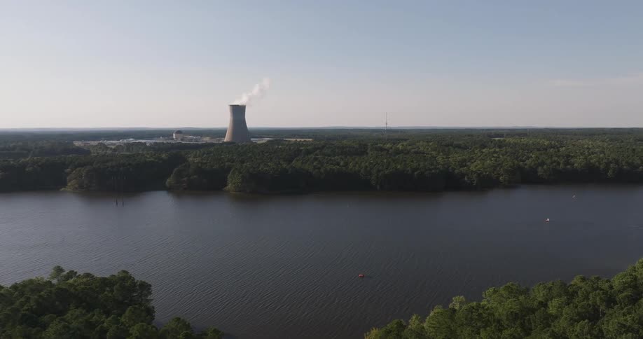 Aerial view of a river surrounded by forest and in the background a large chimney emitting smoke from a factory
