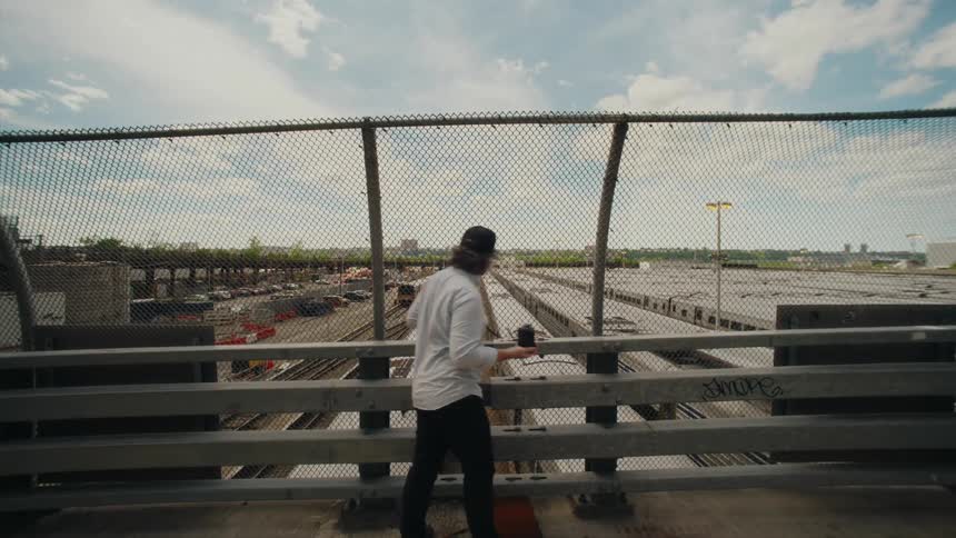 A man stands on a overpass and takes a photo of trains in a station