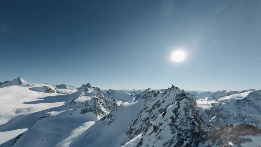 Aerial view of snowy mountain ranges and cliffs with a sun on the horizon in switzerland
