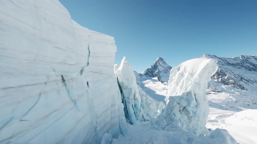 Ice forms crevices on the edge of a glacier overlooking a mountain range on a sunny day