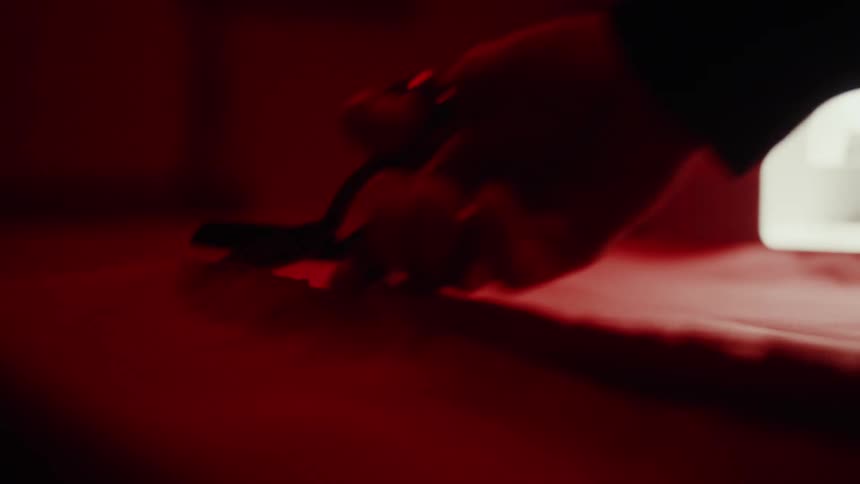 A persons hands holding scissors to cut a piece of fabric and the entire environment around them is lit with a reddish light