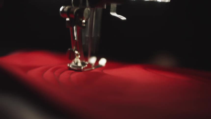 A close up shot shows a sewing machine needle stitching red fabric