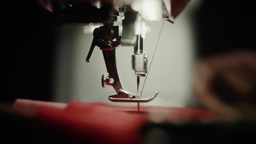 Hands working with red fabric on a manual sewing machine