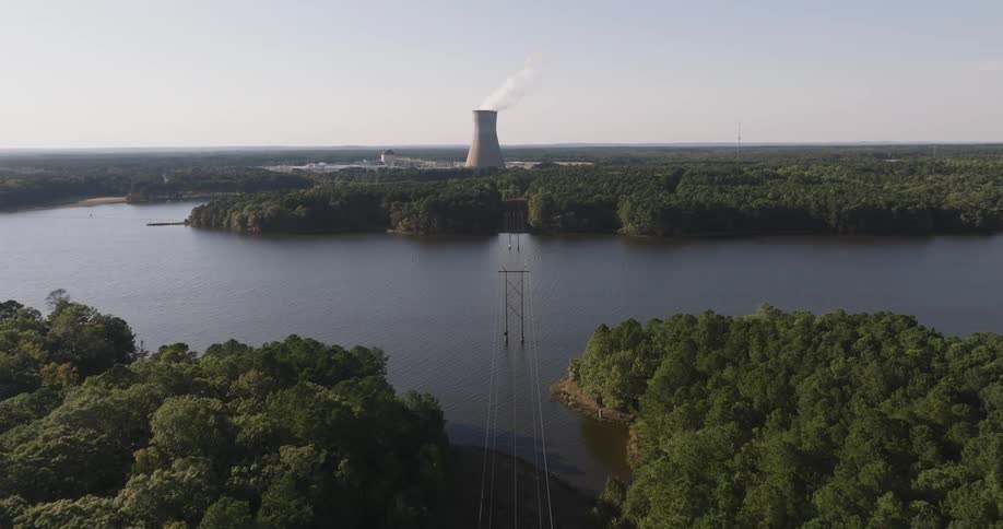 An aerial view of some power line towers passing through forests and trees and a huge river