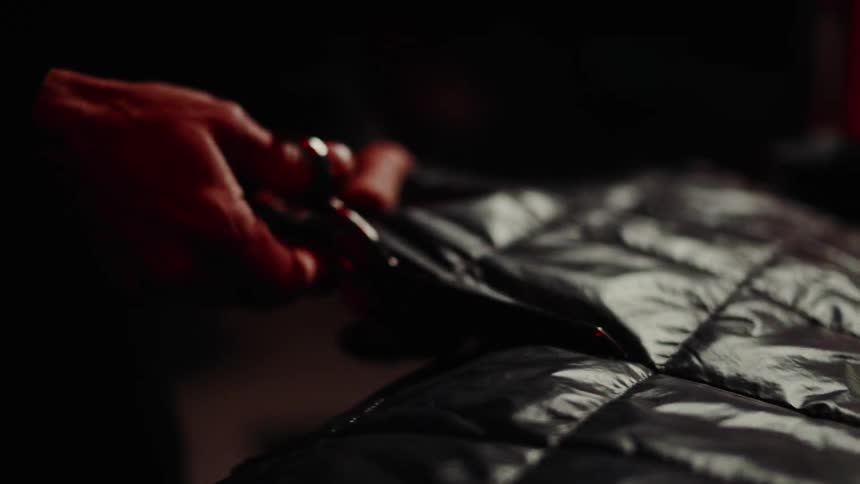Person standing in a dimly lit room cuts quilted fabric with scissors