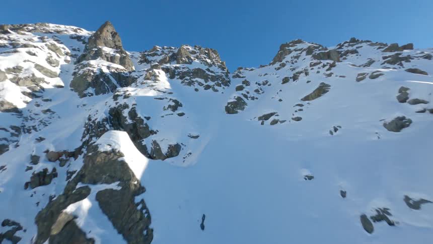 Drone shot of a steep snowy mountain slope under a clear blue sky revealing a skier in Switzerland