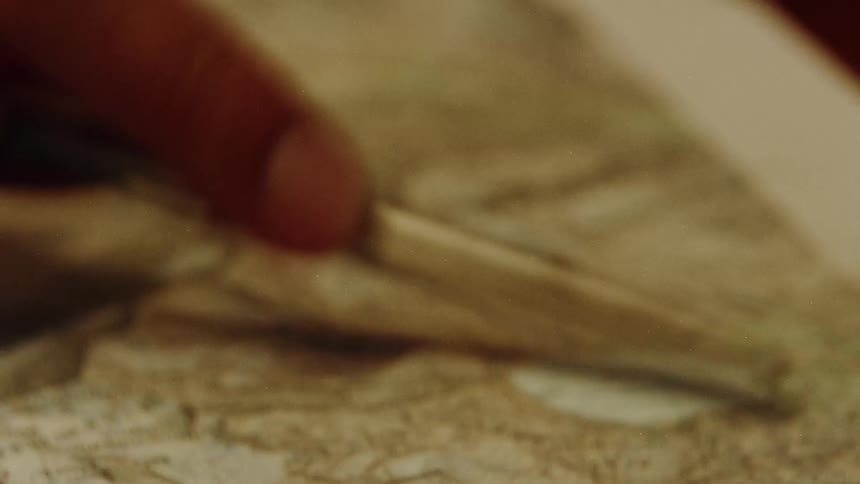 A hand pointing at a location on a vintage map with a gold pen