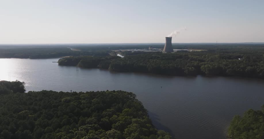 Aerial scene of a river surrounded by forested areas and in the background a large factory chimney