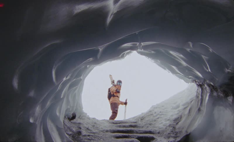 A climber emerges from a dramatic ice cave with a backpack and gear
